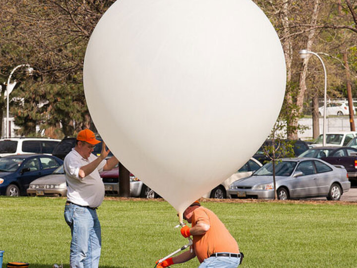 two men blowing up a weather balloon in a field